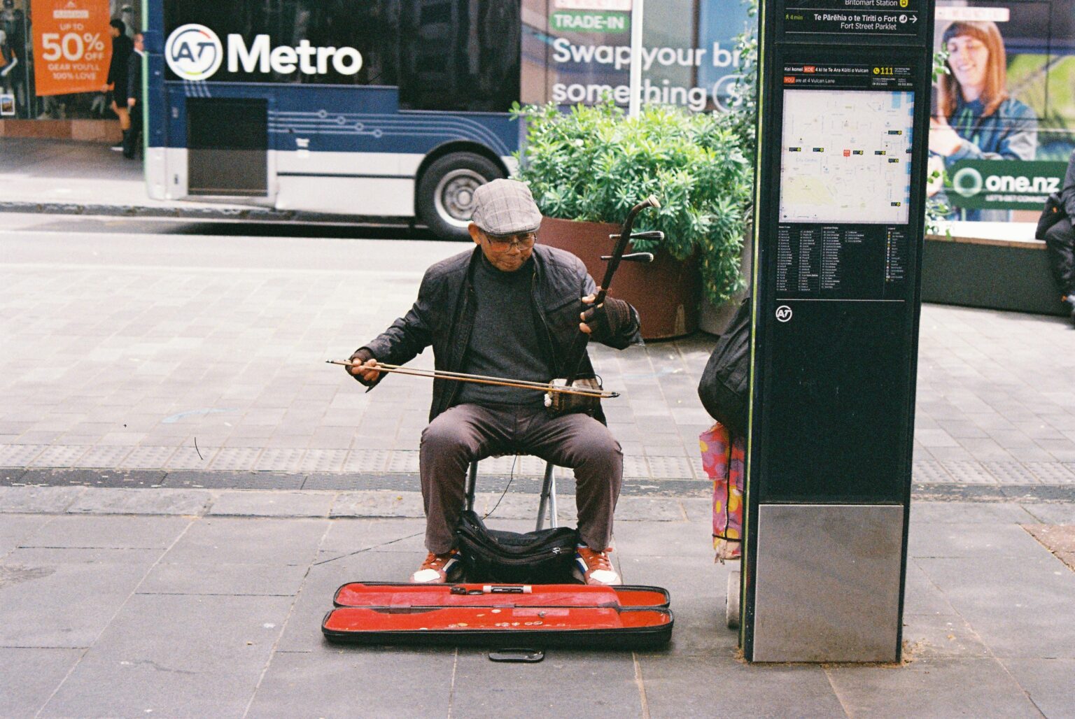 About A street musician playing a traditional string instrument on a city pavement, shot on film