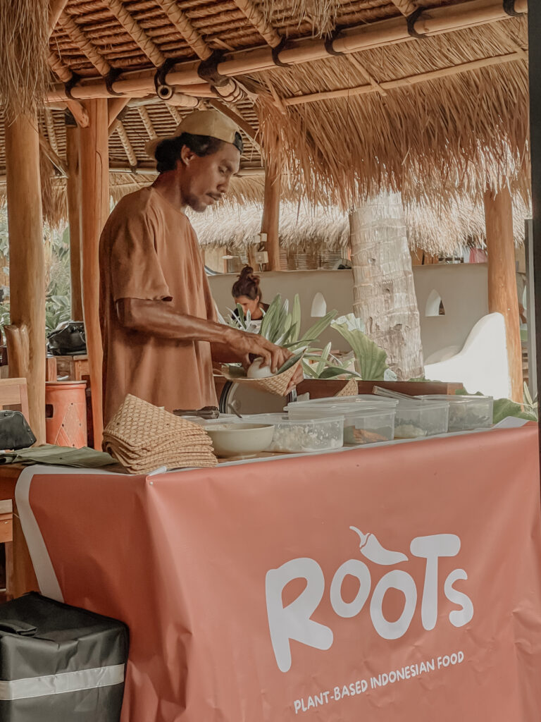 Home A cook preparing plant-based Indonesian food at a market stall under a thatched roof