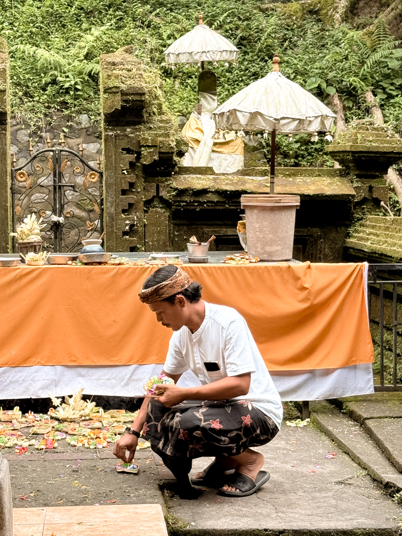 Home A man kneeling to arrange offerings and incense in front of a Balinese temple shrine