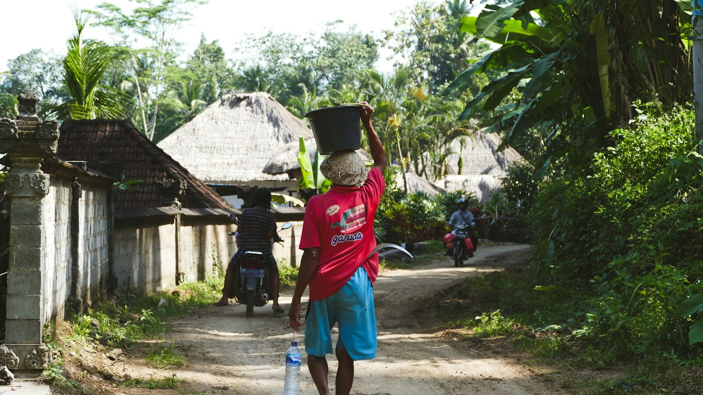 Home A man walking along a dirt road carrying a load, Bali