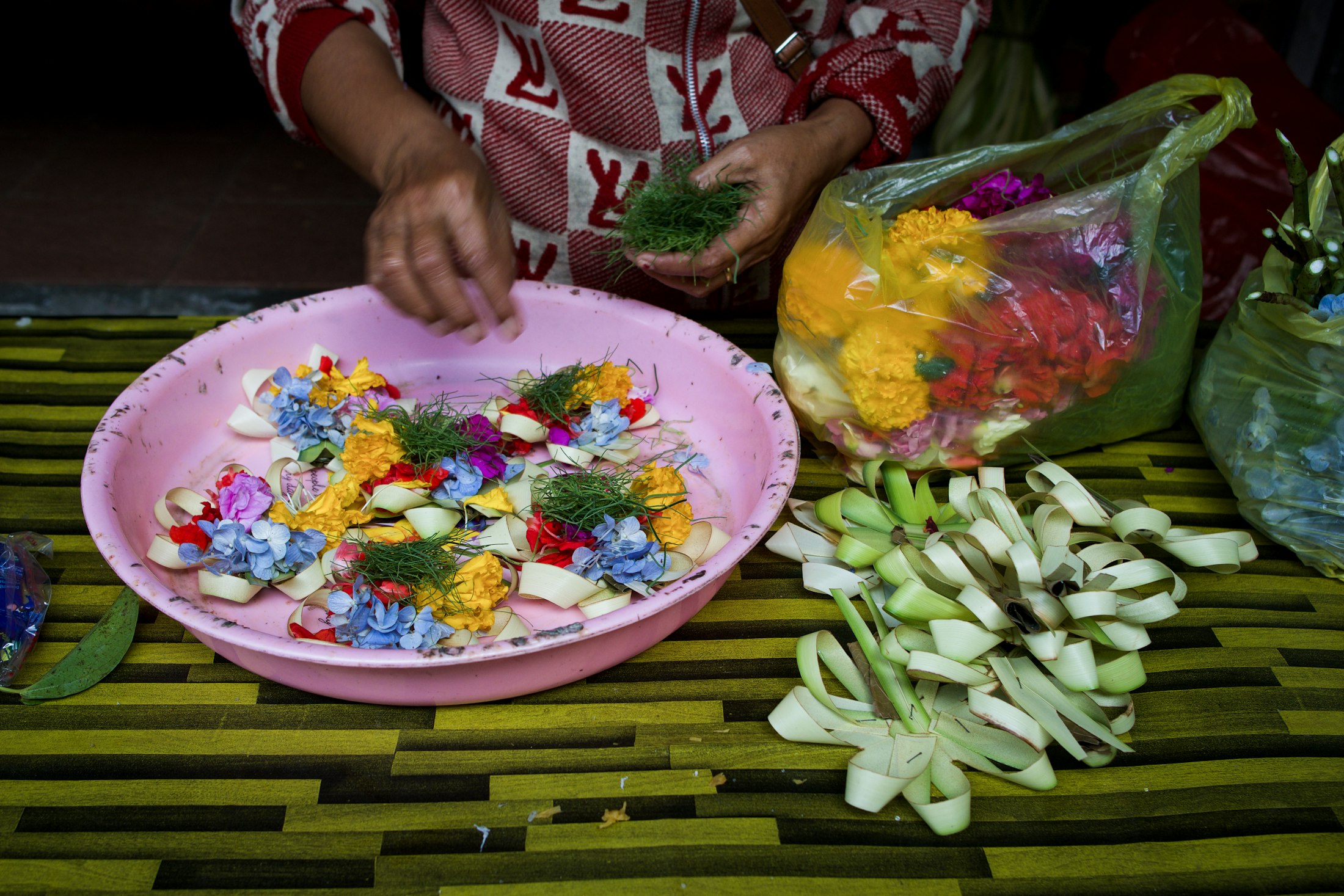 Travel Design Hands preparing canang offerings with flowers and woven palm leaves in Ubud, Bali
