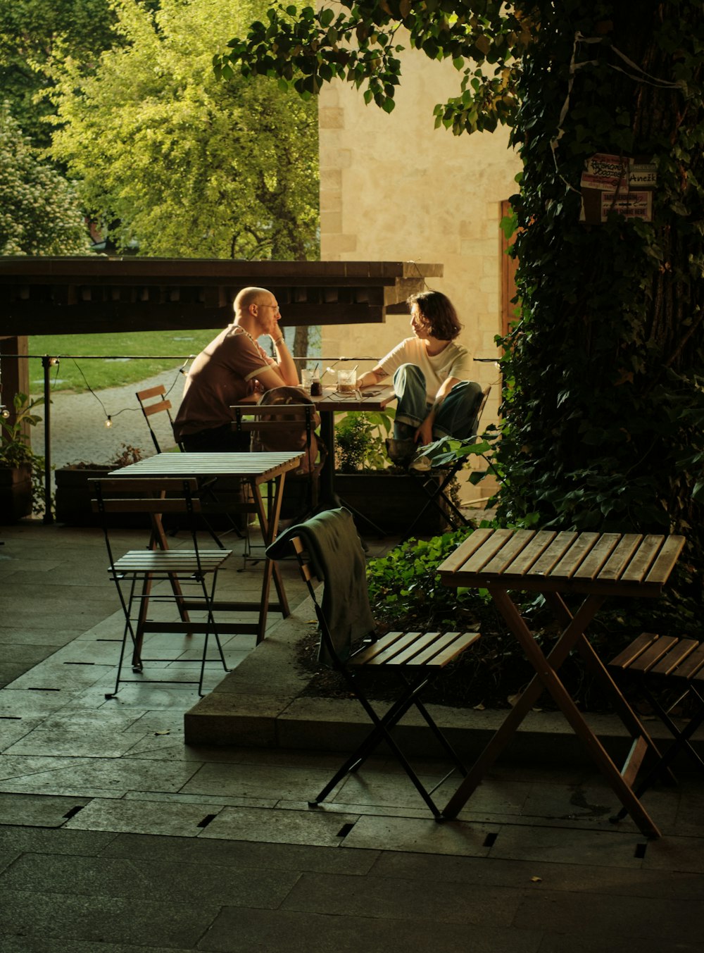 Home Two people talking at a table on a garden patio in the late afternoon light